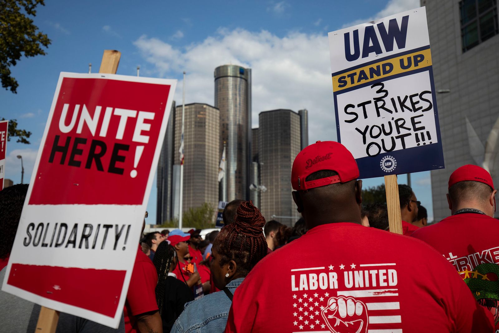 UAW union members strike holding signs with the city in the background.
