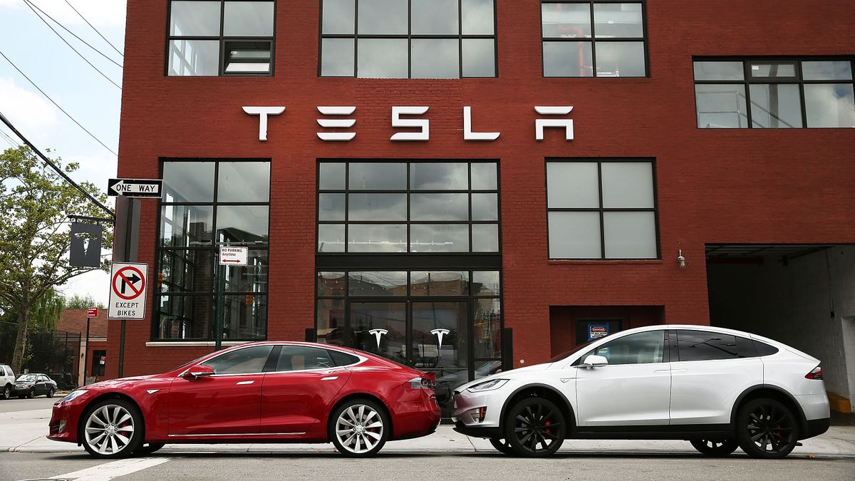 Red and white Tesla cars are parked in front of a brick showroom in Brooklyn with a Tesla sign on the building.