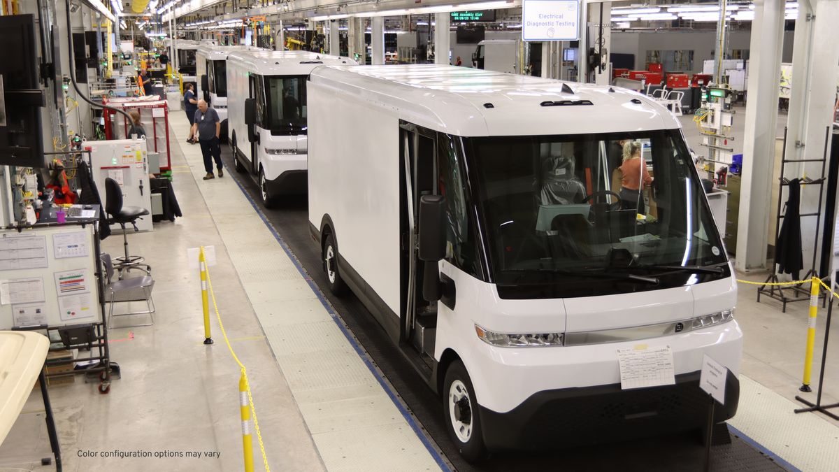 A line of white cargo vans along an assembly line.